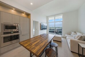 Eine moderne Küche mit eingebauten Geräten, ein Essbereich mit einem Holztisch und ein Wohnzimmer mit einer Couch und großen Fenstern.