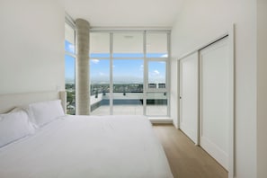 Un dormitorio con una cama grande, una puerta corrediza al balcón y vistas de la ciudad.