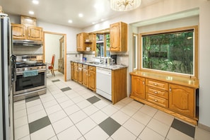 A kitchen with wooden cabinets, a stove, a sink, and a window with a view of greenery. - Nice 3 Bedroom Double Garage Fully Fence Yard Close to Stempede 10 mins to DT (Calgary)