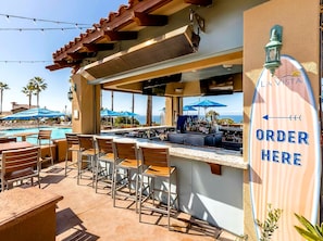 Angolo bar con vista piscina, posti a sedere all'aperto e un cartello che indica il punto d'ordinazione.