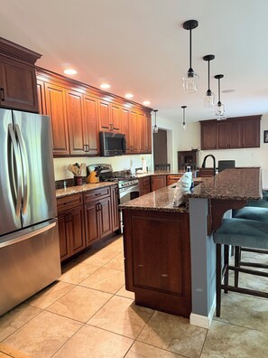 A modern kitchen with wooden cabinets, stainless steel appliances, granite countertops, and pendant lighting. - The Perfect Location in Saratoga Springs (Saratoga Springs)