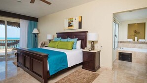 A hotel room with a bed, a desk, a chair, a lamp, a phone, a painting, a bathroom with a bathtub, and a view of the ocean. - CHRISTMAS WEEK / Cancun 3BR Oceanfront Resort (Cancún)
