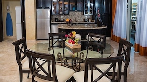 A dining area with a glass table, dark wooden chairs, a chandelier, and a kitchen in the background. - CHRISTMAS WEEK / Cancun 3BR Oceanfront Resort (Cancún)