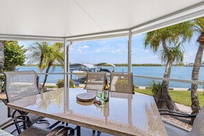 Een overdekt terras met eethoek, een glazen tafel, stoelen en uitzicht op het water.