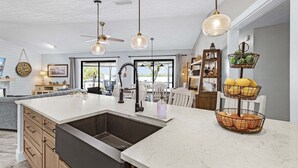 Una cucina moderna con una grande isola, luci a sospensione e un cestino di frutta a più livelli.