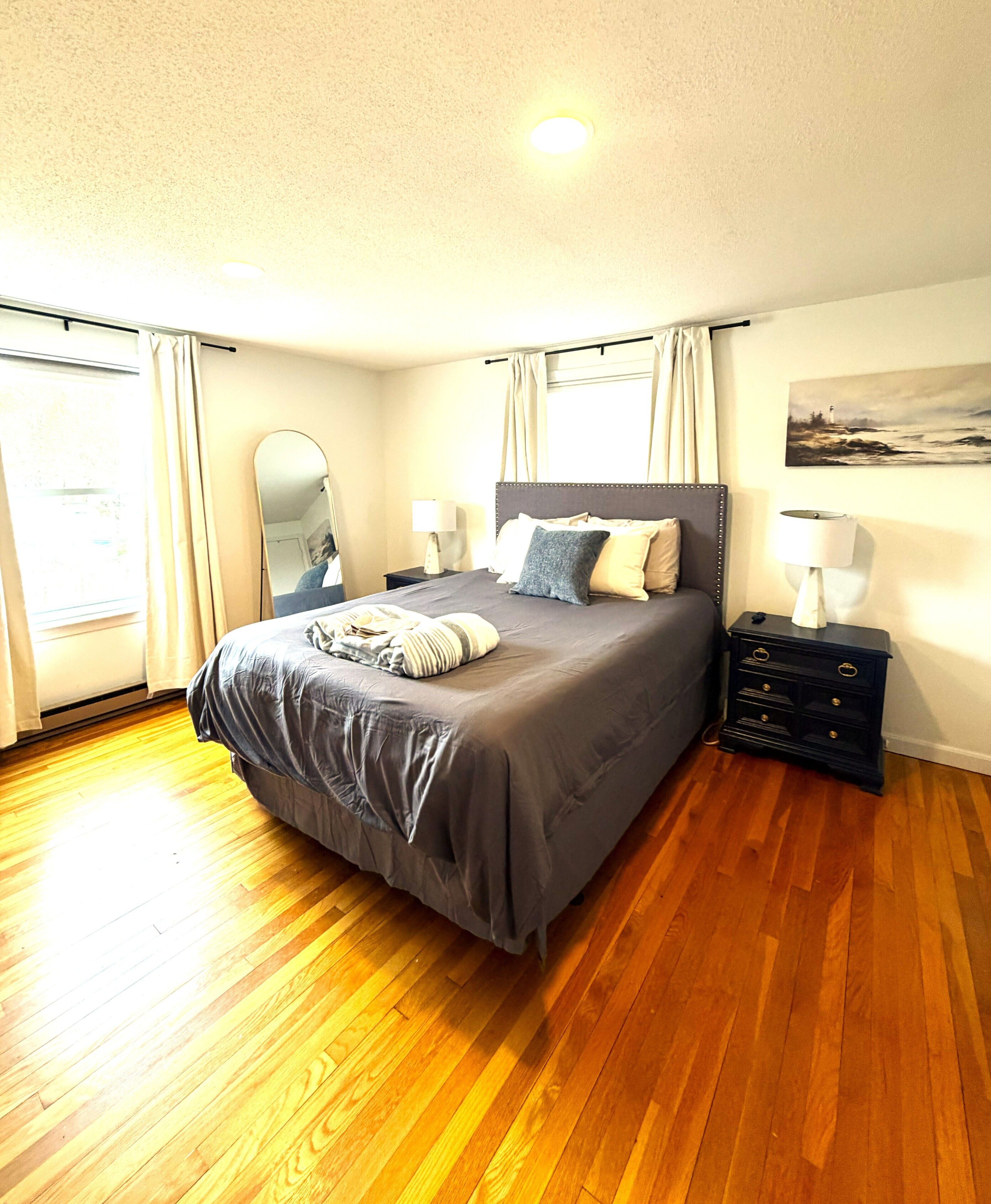 A bedroom with a large bed, a bedside table with a lamp, a mirror, and a painting on the wall.