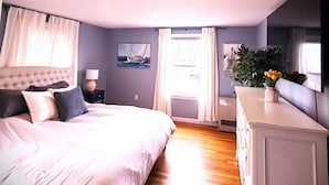 Una camera da letto con un letto, un comodino, una cassettiera, una finestra con tende e un quadro appeso al muro.