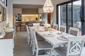 A dining area with a long table, white chairs, and a chandelier.
