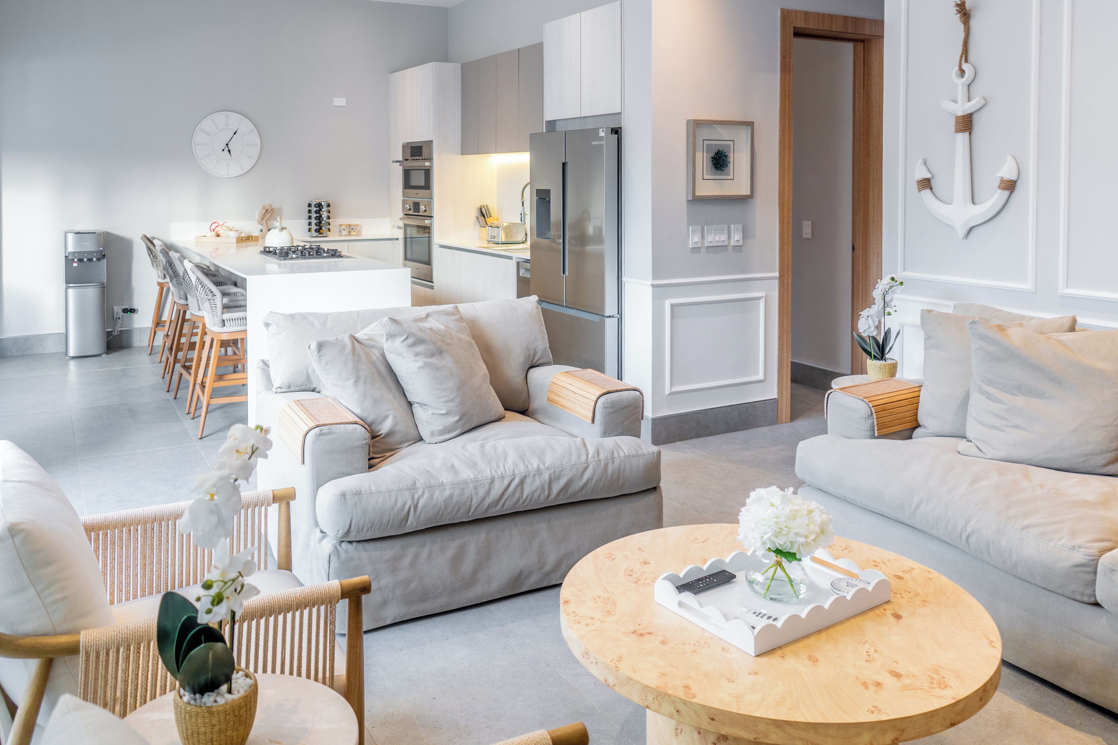 Una sala de estar moderna con sofá, sillas, una mesita de centro y una cocina con refrigerador y juego de comedor.