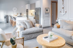 A modern living room with a sofa, chairs, a coffee table, and a kitchen area with a refrigerator and dining set.