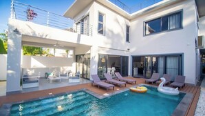 Ein modernes Haus mit Pool, Sitzgelegenheit im Freien und einem Balkon.