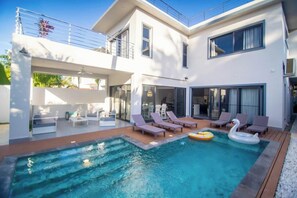 A modern house with a swimming pool, outdoor seating, and a balcony.