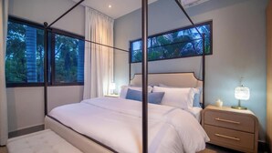 Ein Schlafzimmer mit Baldachinbett, Nachttisch mit Lampe und Blick auf Bäume durch das Fenster.