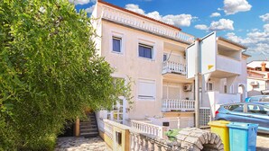 Ein Gebäude mit Balkon, Mülltonnen und einem geparkten Auto.
