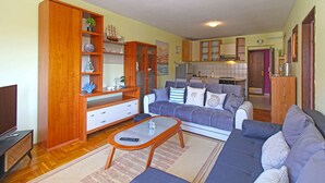 Ein Wohnzimmer mit Sofa, Couchtisch, Fernseher, Holzböden und einer Küchenzeile im Hintergrund.