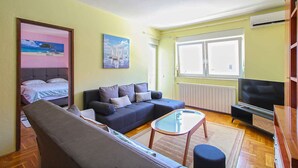 Ein Wohnzimmer mit Sofa, Couchtisch, Fernseher und Fenster.