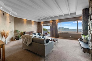 A spacious living room with a large window, a stone fireplace, and a view of the landscape.