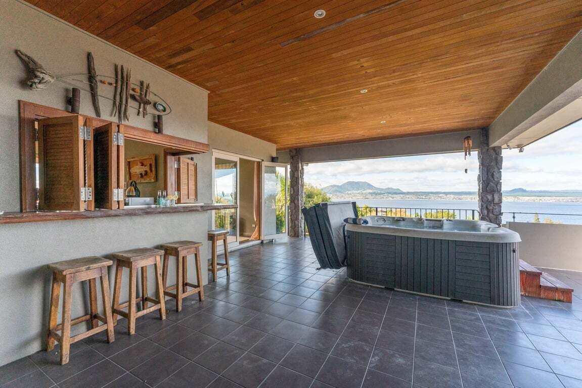 A covered outdoor area with a hot tub, wooden stools, and a view of a body of water.
