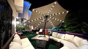 Un espace extérieur aménagé avec des sièges, un grand parasol, des meubles en osier et un foyer.