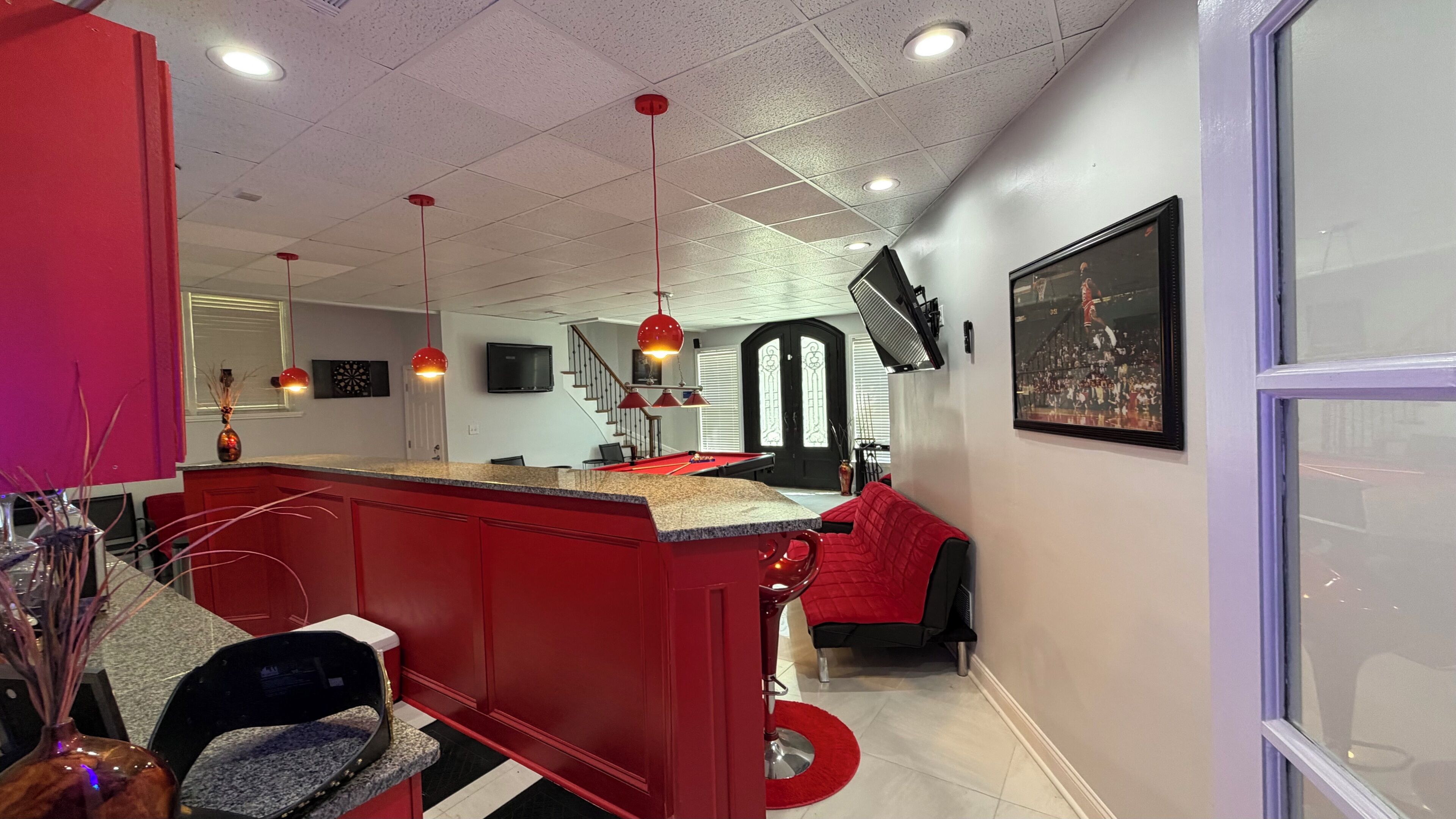 A modern interior with a pool table, red accents, a staircase, and a framed picture on the wall.