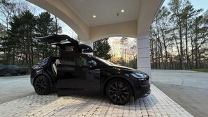 Musta auto oli pysäköitynä valkoisen rakennelman alle, ja sen alla oli asfaltoitu alue.