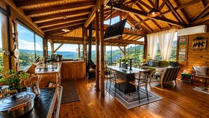 A wooden interior with a dining area, kitchen, and seating area with a view. - Country house in the mountains of Santa Catarina, at 1000m altitude, surrounded by nature. (Alfredo Wagner)