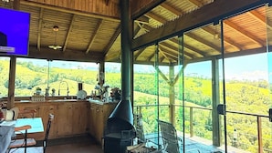 A wooden interior with a large fireplace, a dining area, and a view of the countryside. - Country house in the mountains of Santa Catarina, at 1000m altitude, surrounded by nature. (Alfredo Wagner)