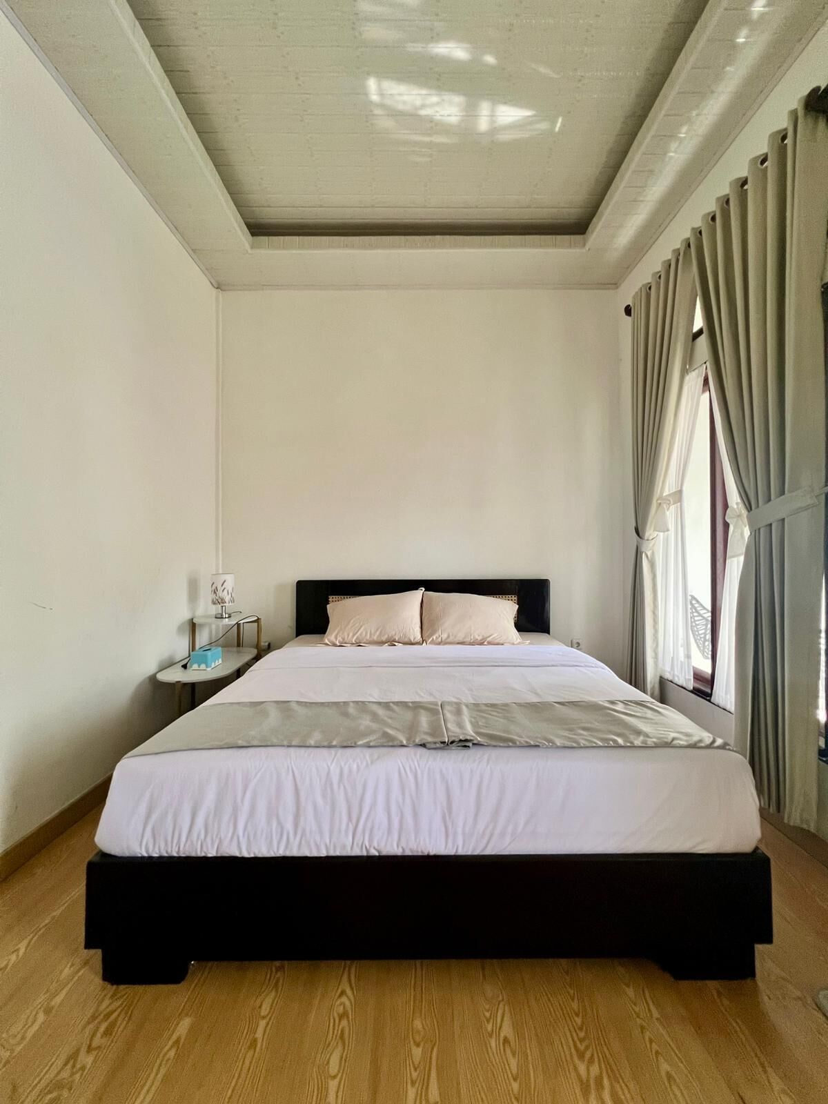 A bedroom with a large bed, a nightstand, a lamp, and a window with curtains.