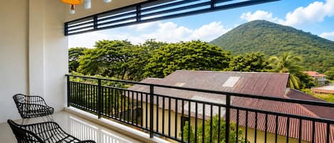 A balcony with a view of a mountain, two chairs, and a hanging light fixture.