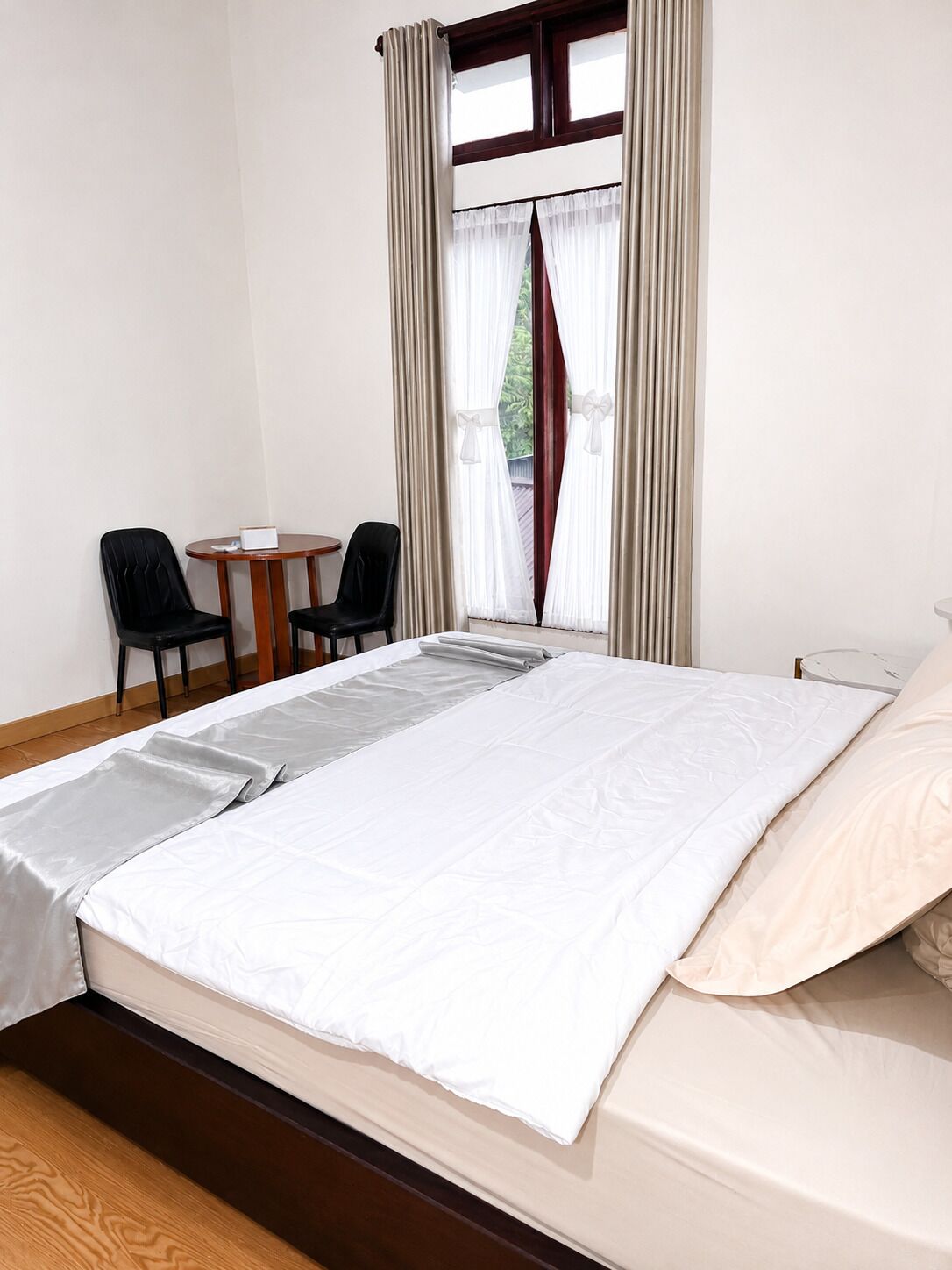 Una habitación de hotel con cama, dos sillas, una mesita y una ventana con cortinas.