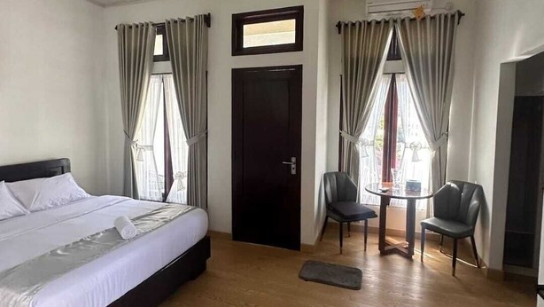 A hotel room with a bed, two chairs, a small table, and a door. - D' Kabong SIRIH Homestay (Bandanaira)