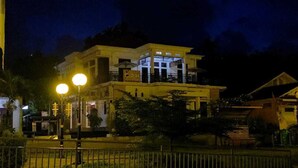 A two-story building with a balcony, illuminated by street lamps, surrounded by greenery. - D' Kabong SIRIH Homestay (Bandanaira)