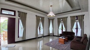 A spacious living room with a large sofa, a coffee table, and a chandelier. - D' Kabong SIRIH Homestay (Bandanaira)