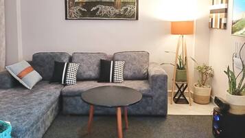 A living room with a grey sofa, a round coffee table, a lamp, and a painting on the wall.