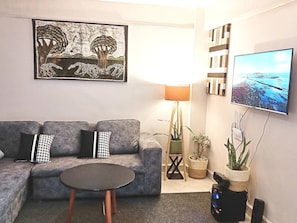 A living room with a grey sofa, a small round table, a floor lamp, a TV, and a painting.