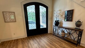 A hallway with a wooden floor, a black door with decorative glass panels, a console table with vases, and two framed artworks on the wall. - Spacious Modern Home on Acreage (Melissa)