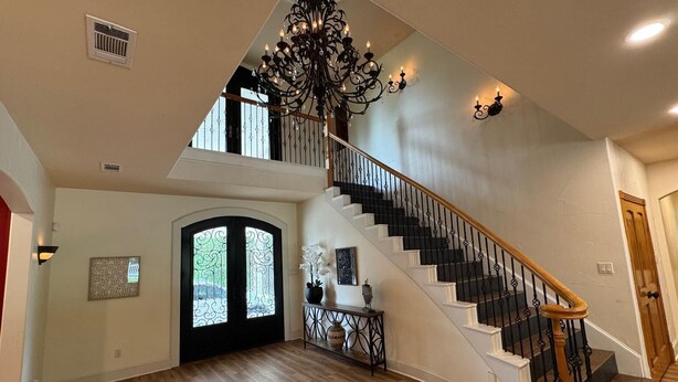A spacious foyer with a wooden floor, a grand staircase with black balusters, and a chandelier. - Spacious Modern Home on Acreage (Melissa)