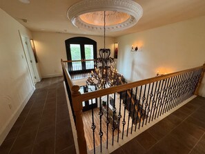 A spacious interior with a grand chandelier, a wooden staircase railing, and a view of the outdoors through a large window. - Spacious Modern Home on Acreage (Melissa)