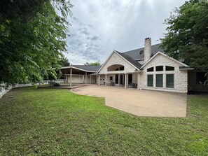 A two-story stone house with a covered patio, a stone chimney, and a fenced yard. - Spacious Modern Home on Acreage (Melissa)