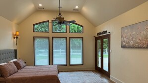 A bedroom with a bed, a ceiling fan, large windows, a door, and a painting on the wall. - Spacious Modern Home on Acreage (Melissa)