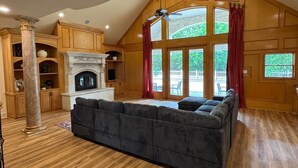A spacious living room with a fireplace, wooden paneling, and large windows. - Spacious Modern Home on Acreage (Melissa)