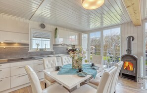 A modern kitchen with white cabinetry, a dining area with a table set for two, and a wood-burning stove. - 3 bedroom awesome home in Wandlitz (Wandlitz)