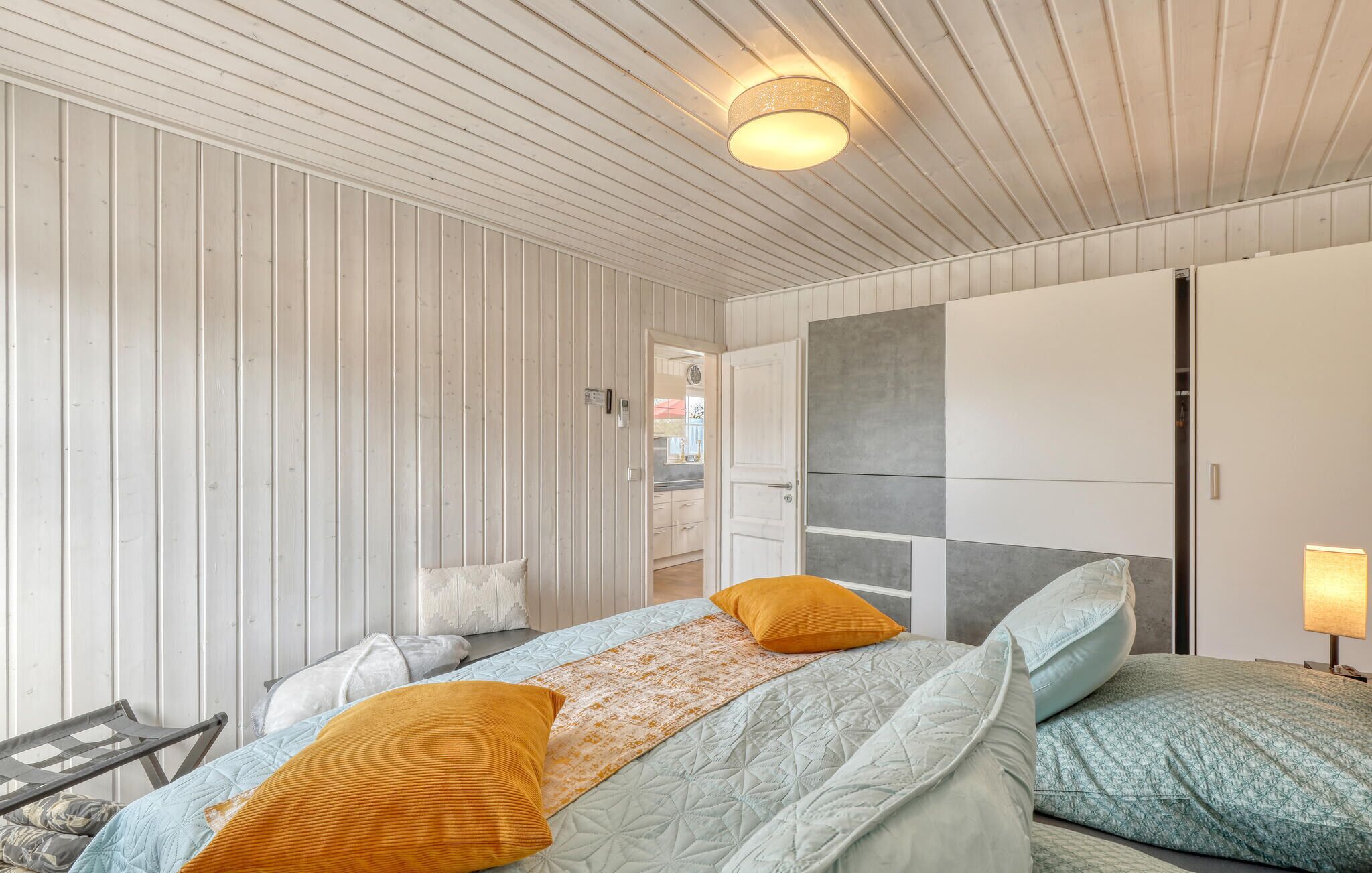 Un dormitorio con cama, almohadas, mesita de noche, lámpara y armario.