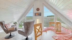 A cozy attic room with a sloped ceiling, a large window with a view of the countryside, a clock, and a table with a lantern. - Cozy home in Wandlitz with WiFi (Wandlitz)