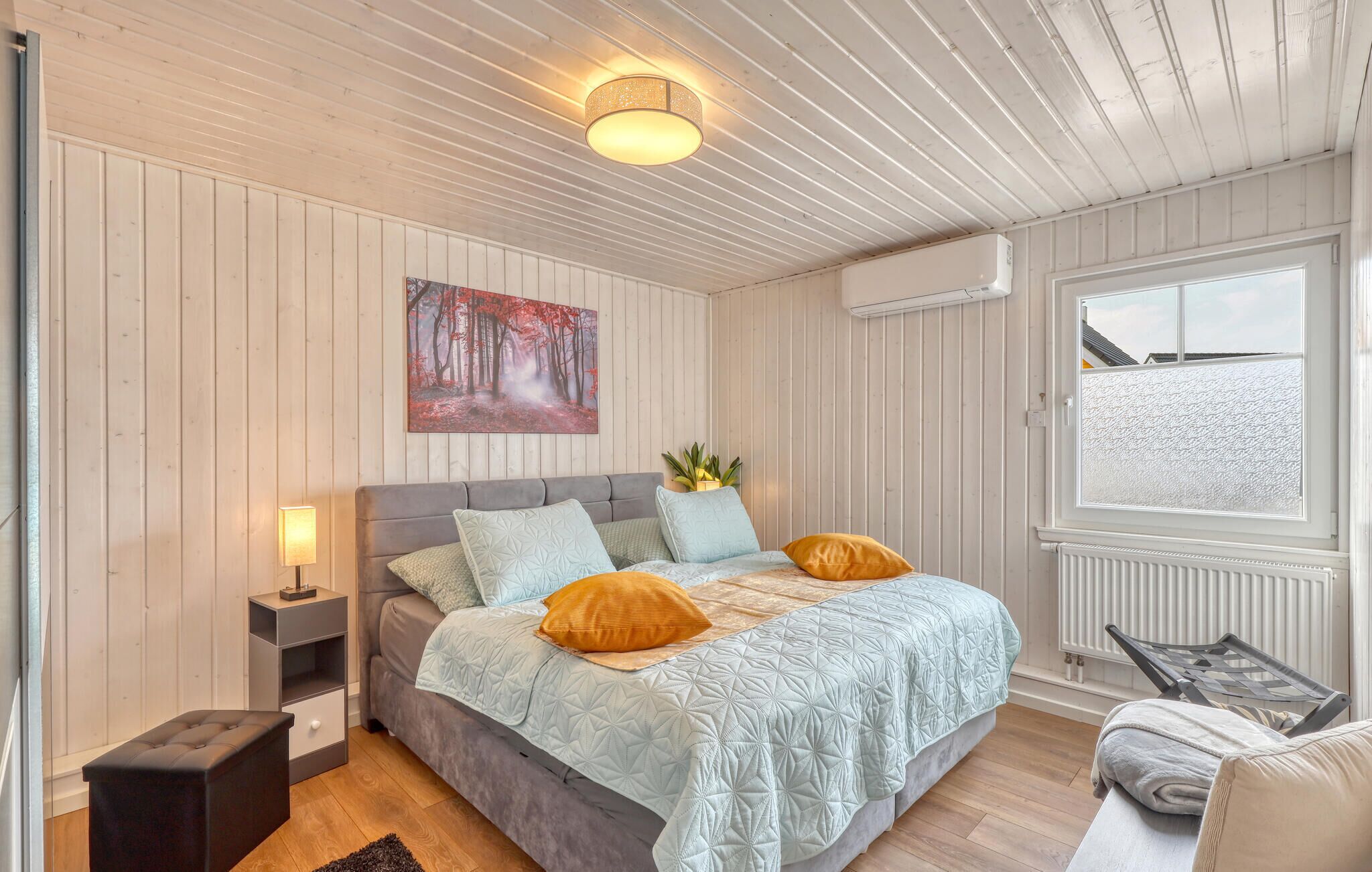 Et soveværelse med seng, sengebord, lampe og et vindue med udsigt.