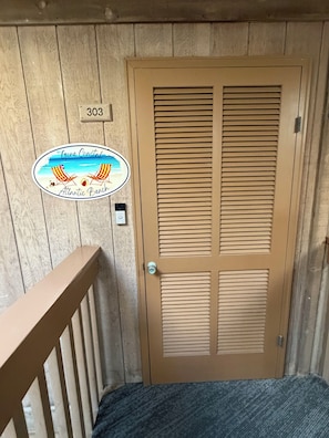 A wooden door with a number plate, a beach-themed sticker, and a small light switch.