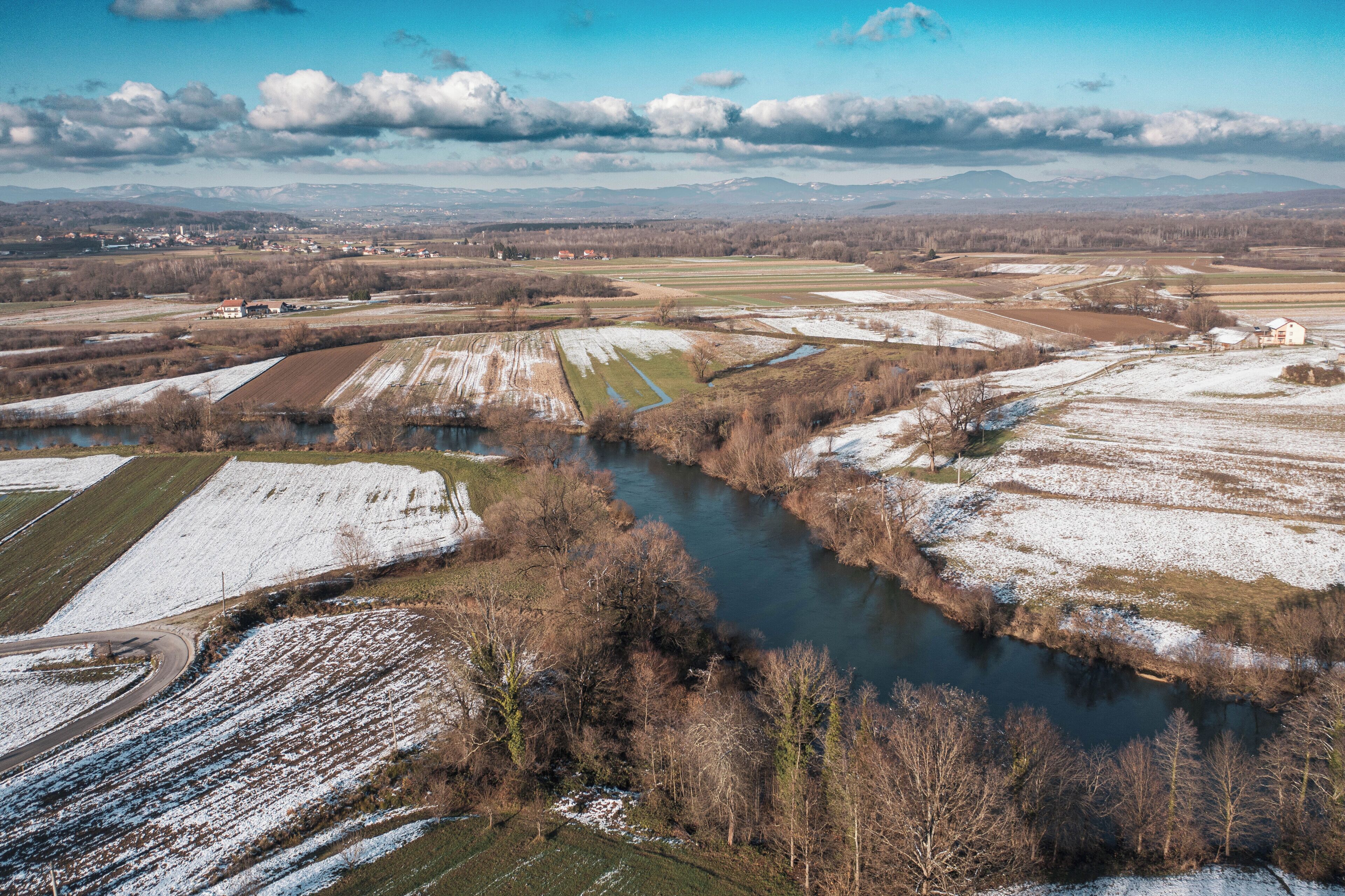 Une rivière qui traverse des champs enneigés, avec des montagnes qui se dessinent à l'horizon.