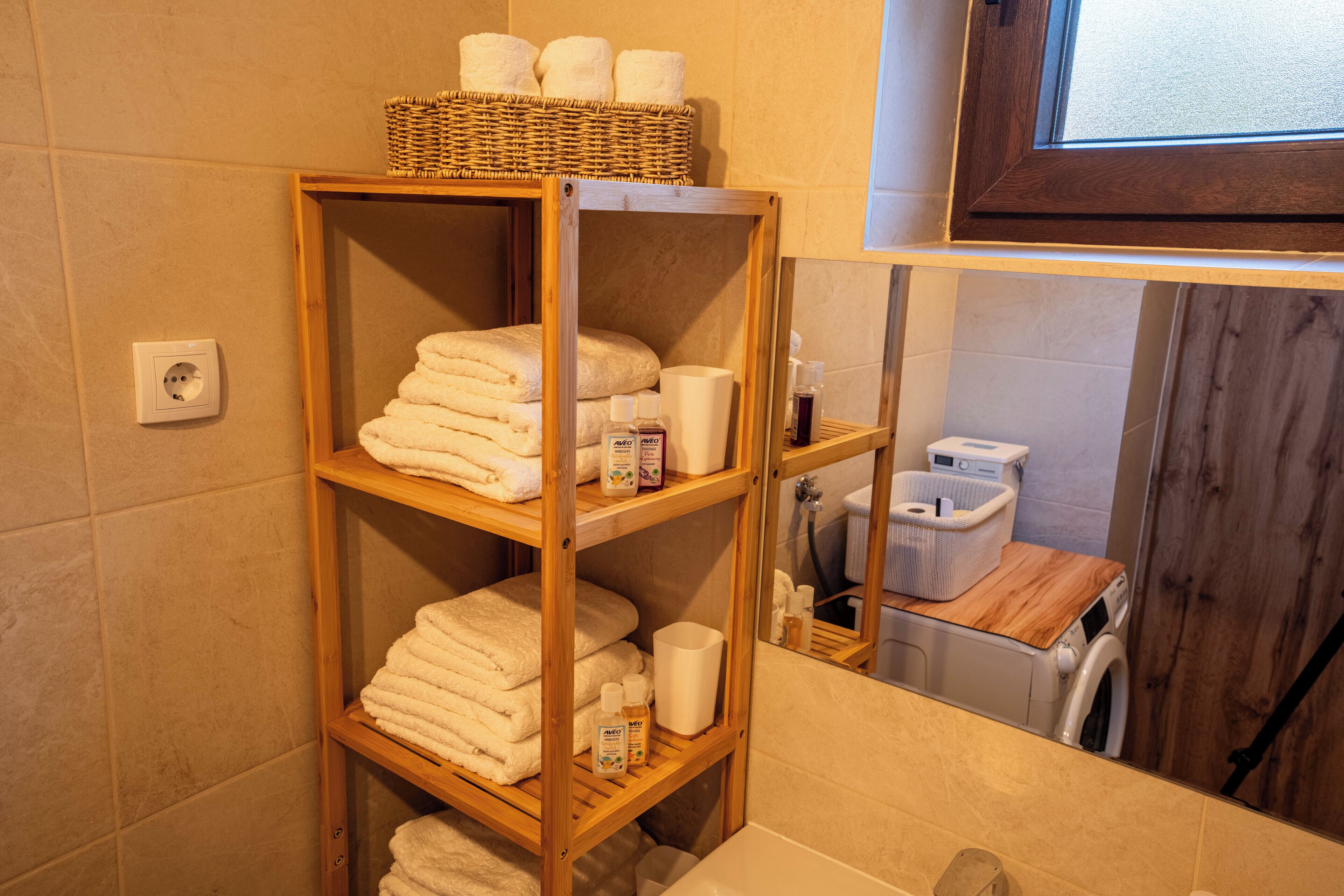 Un baño con repisas de madera que sostienen toallas y artículos de aseo, una lavadora y un espejo que refleja el ambiente.