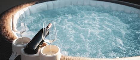 A hot tub with two glasses and a bottle, surrounded by wicker furniture.