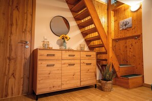 Una escala de fusta, un armari de fusta amb calaixos, un mirall rodó i un ram de flors.